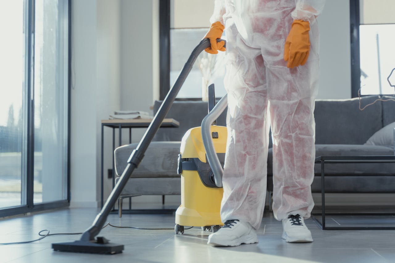 expertise-01 A cleaner in protective coveralls and gloves vacuuming a modern living room.